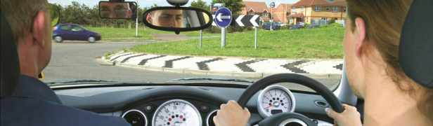 Cabin view over shoulder of learner and instructor waiting at roundabout.